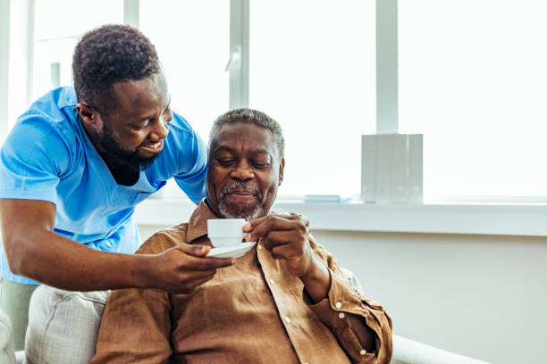 Smiling male nurse serving the cup of coffee to elderly smiling man